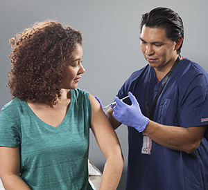 Proveedor de atención médica aplicándole una inyección a una mujer en el brazo.